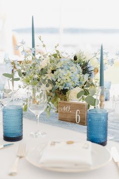 the table is set with blue and white flowers, candles, and napkins on it