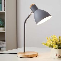 a desk lamp sitting on top of a white table next to a potted plant