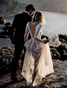 a man and woman standing on top of a rocky hill next to the ocean holding hands