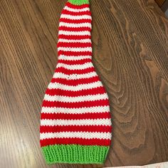 a knitted red and green hat sitting on top of a wooden table next to a piece of paper