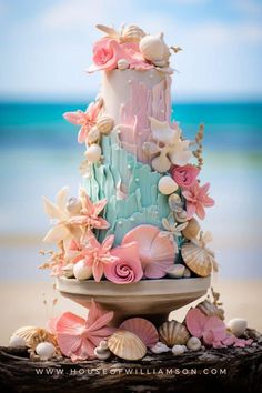 a three tiered cake with seashells and flowers on the top is decorated in pastel colors