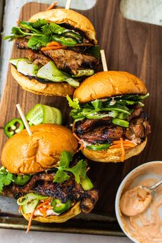 three hamburgers with lettuce, pickles and carrots on a cutting board