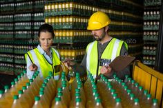 two workers standing in front of rows of yellow and green bottles with one holding a clipboard