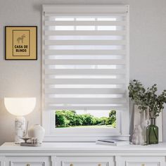 a white window with blinds on top of it in front of a desk and lamp