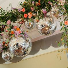 disco balls hanging from the ceiling with flowers and greenery in them on top of a mantel