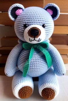 a crocheted teddy bear with a green ribbon around it's neck sitting on a table