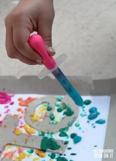 a child's hand holding a pink and blue toothbrush in front of an art project