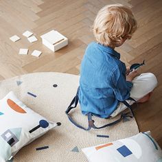 a little boy sitting on the floor playing with some blocks and pillows in front of him