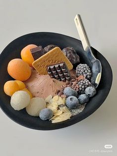 a black bowl filled with assorted fruits and desserts on top of a white table