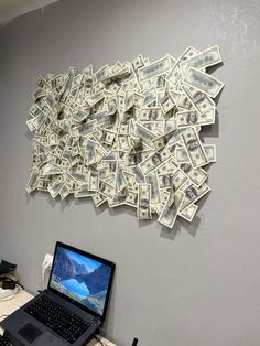 a laptop computer sitting on top of a wooden desk next to a pile of money