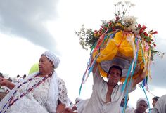 some people are walking down the street with flowers on their head and one is carrying something over his head