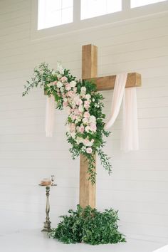 a cross decorated with flowers and greenery in front of a white wall at a wedding