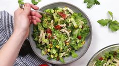 a person holding a fork in a bowl filled with lettuce, corn and tomatoes