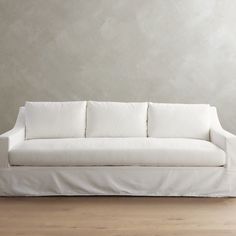 a white couch sitting on top of a hard wood floor next to a gray wall