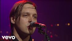 a man singing into a microphone while standing in front of a purple and red background