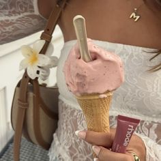 a woman holding an ice cream cone with pink frosting on it and a tube of lip balm