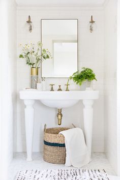 a white sink sitting under a mirror next to a basket filled with flowers and plants