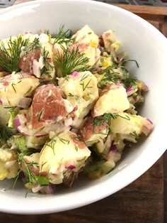 a white bowl filled with potato salad on top of a wooden cutting board