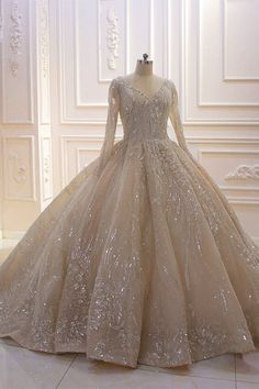 a wedding dress on display in a room with white walls and flooring, it has long sleeves that are embellished with sparkling sequins