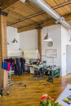 an office with wooden floors and lots of clothes hanging from the ceiling, along with two desks