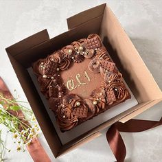 a square cake in a box with the number one on it and flowers next to it