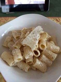 a white bowl filled with pasta on top of a table next to a tablet computer