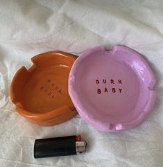 two orange and pink bowls with the words burn baby written on them next to a lipstick bottle