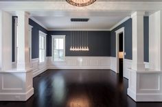 an empty living room with blue walls and white trim around the windows, chandelier hanging from the ceiling