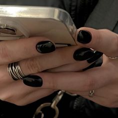 a woman with black nail polish holding a cell phone in her right hand and gold rings on her left wrist