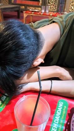 a man leaning over with his head on the table next to a drink and cell phone