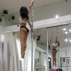 two women in bikinis hanging upside down on the side of a pole with mirrors behind them