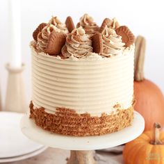 a frosted cake sitting on top of a white plate next to two pumpkins