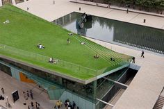 people are walking around in front of a building with a green roof and grass on top