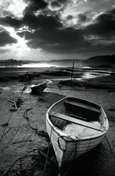 a boat sitting on top of a sandy beach next to the ocean under a cloudy sky