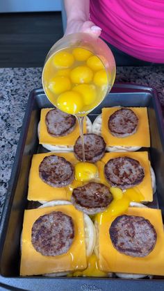 someone is pouring orange juice on some cheese and sausages in a baking pan with other food items