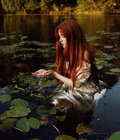 a woman with long red hair sitting in the water holding a frog's hand