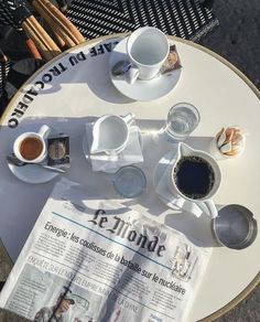 two cups of coffee are sitting on a table with newspaper and utensils next to it