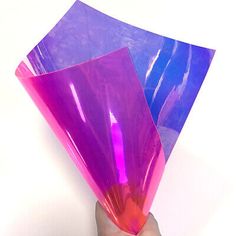 a hand is holding three purple and blue pieces of plastic wrapper on top of each other