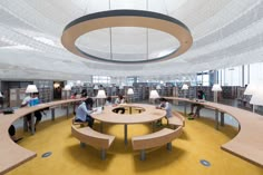 people are sitting at tables and reading books in an open area with circular lights on the ceiling