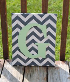 a canvas with the letter g painted on it sitting on a wooden deck in front of some grass