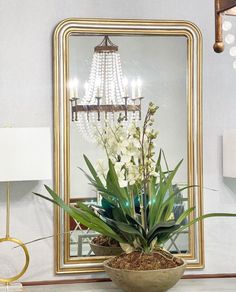 a vase with flowers in it sitting on a table next to a mirror and chandelier