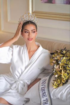 a woman wearing a tiara sitting on a bed with flowers in front of her