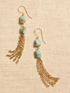 two pairs of earrings with chains and turquoise beads on top of each earring, sitting on a piece of fabric