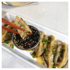 a white plate topped with dumplings covered in sauce and green onions next to chopsticks