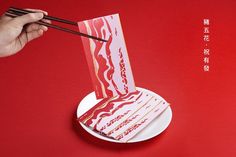 someone holding chopsticks over a piece of paper with food in it on a plate