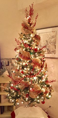 a decorated christmas tree with red and white ribbons on it in a living room area