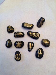 some black and gold painted rocks on a white surface with writing in the middle one has an egyptian symbol