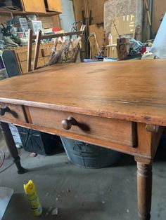 an old wooden table in a garage with tools on the floor and other items around it