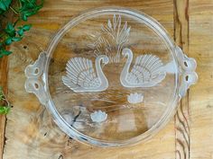 a glass plate with two swans on it sitting on a wooden table next to a plant