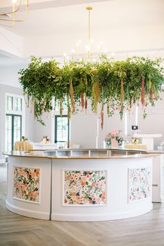 a white counter topped with lots of greenery next to a chandelier filled with candles